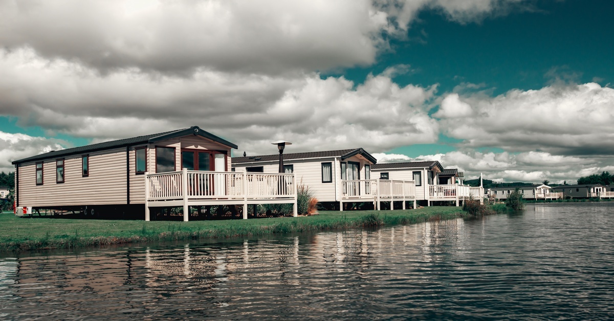 Mobile homes line up along the edge of a large body of water. Each mobile home contains a porch facing the water. Mobile homes line up along the edge of a large body of water. Each mobile home contains a porch facing the water.