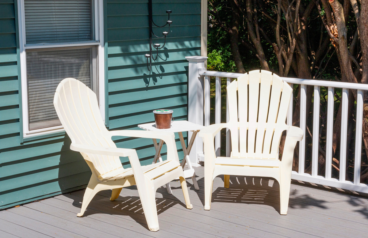 Two white Adirondack chairs and a small table sit on a gray fiberglass deck that's attached to a teal house.