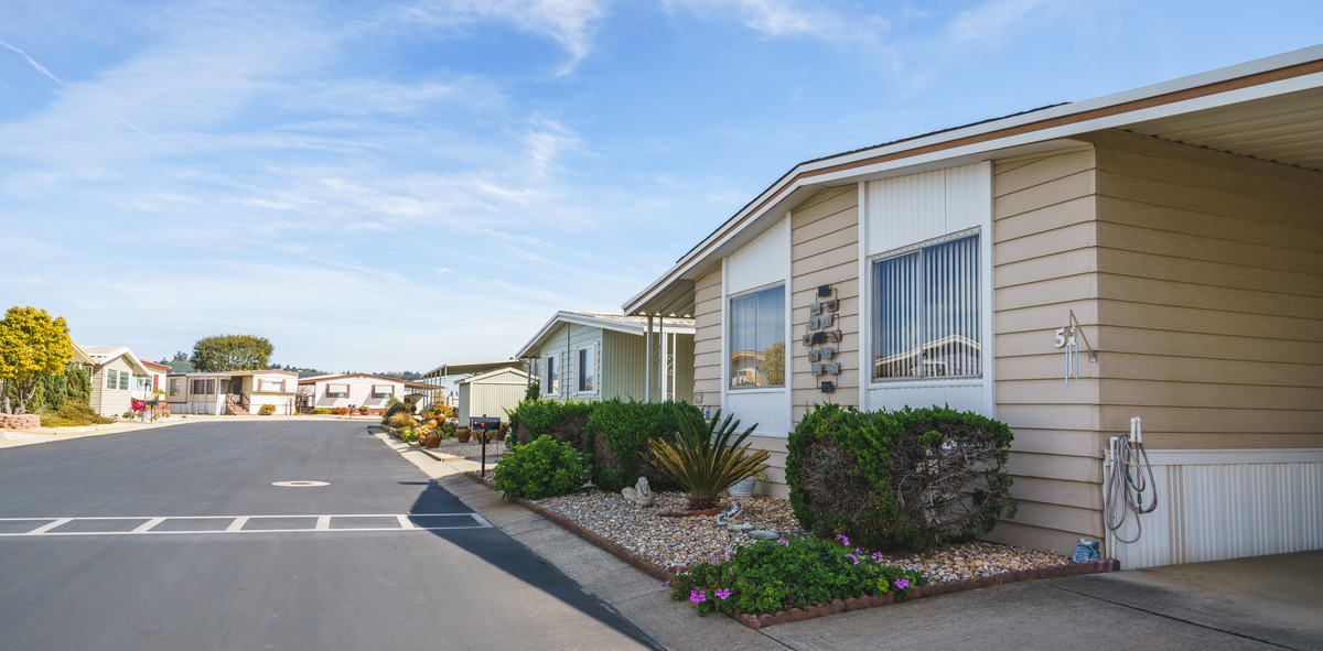 A row of well-maintained manufactured homes with landscaping, sitting along a paved street on a sunny day.