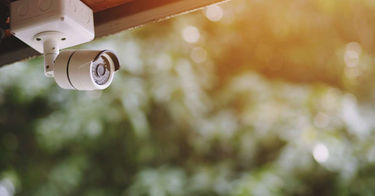 A white home security camera that's part of a security system is mounted on the roof overhang of a home.