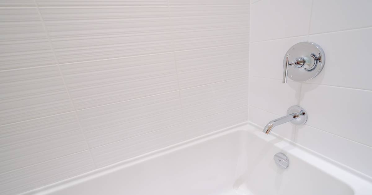 A freshly updated mobile home bathroom features a white standard tub, a tile-look bathtub surround, and chrome fixtures.