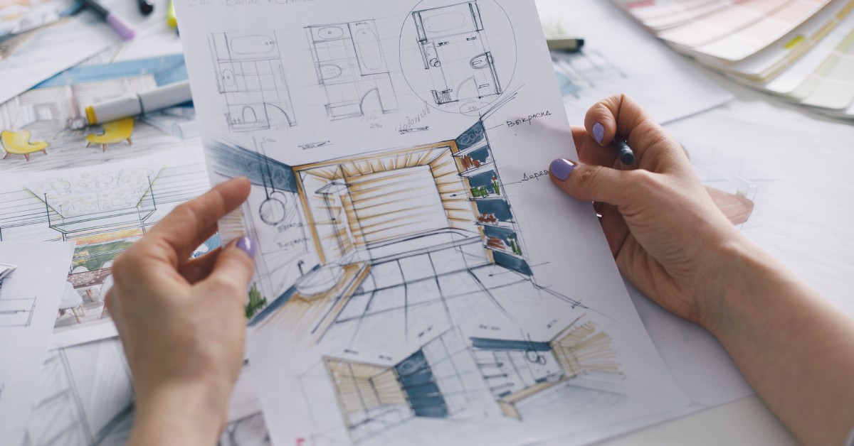 An interior designer holds a colorful sketch of a plan for a bathroom renovation. Markers and paint swatches sit on the desk.