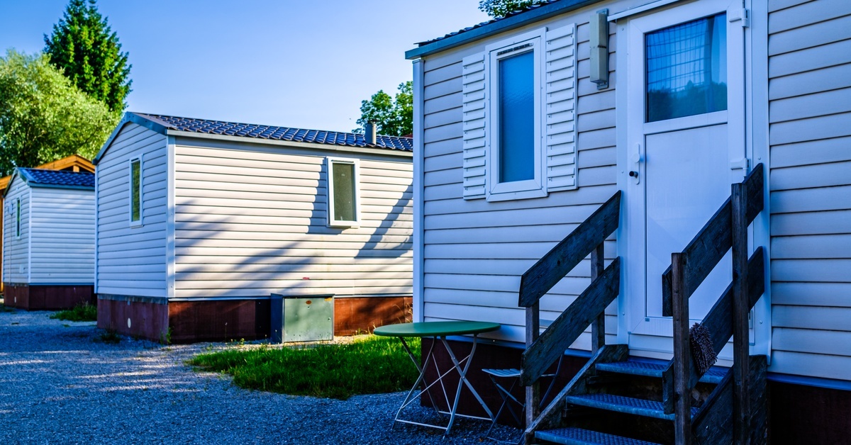 Several small white mobile homes next to one another with gravel and grass around them. Several small white mobile homes next to one another with gravel and grass around them.