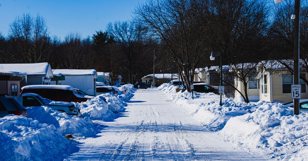 A snow-covered trailer home park has cars parked in the driveways, but the neighborhood road has been cleared. A snow-covered trailer home park has cars parked in the driveways, but the neighborhood road has been cleared.