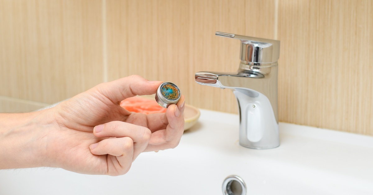 A person holding a bathroom faucet aerator over a white porcelain sink to showcase the sediment buildup.
