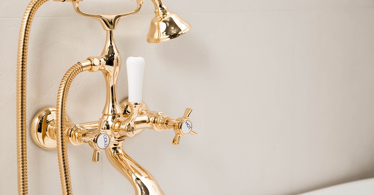 A brass bathtub faucet with a retro design featuring white handles, a handheld sprayer, and labeled hot and cold knobs.