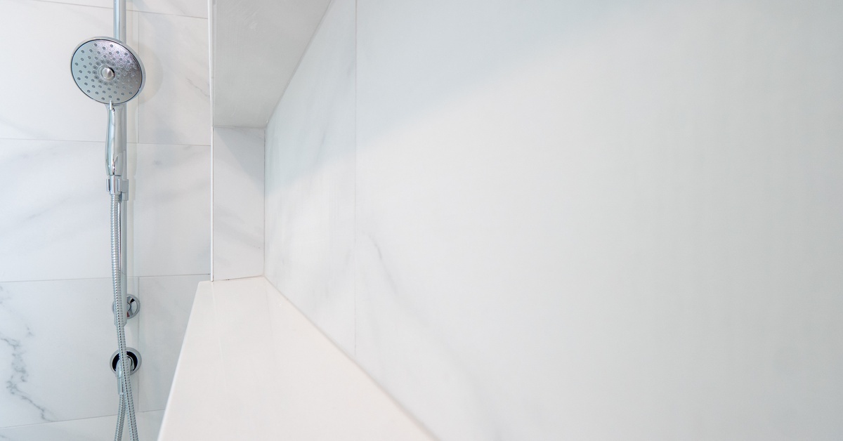 A large shower features clean white tiles, a built-in wall shelf, and an adjustable silver showerhead.