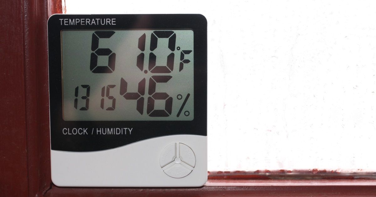 A black-and-white digital hygrometer sits on a red windowsill, displaying 46% humidity and 61 degrees Fahrenheit.