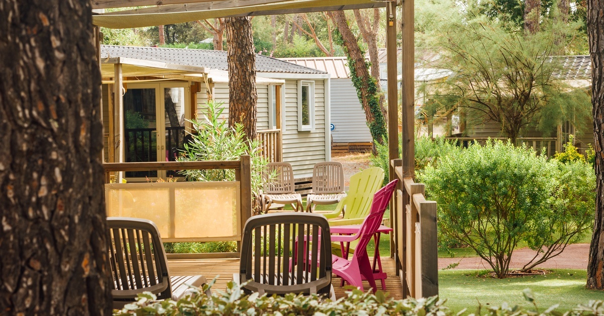 The outdoor areas of a mobile home park feature wooden porches, outdoor furniture, trees, shrubs, and a brick pathway.