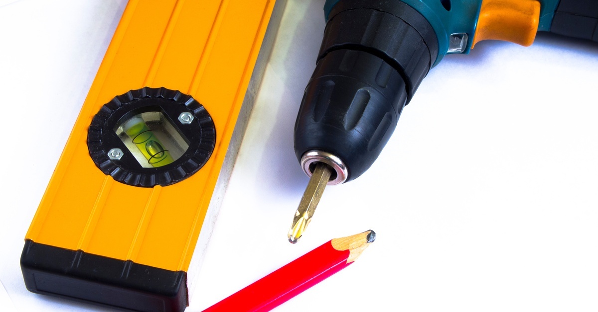 A set of basic tools, including a drill, level, and carpenter’s pencil, arranged on a white background.