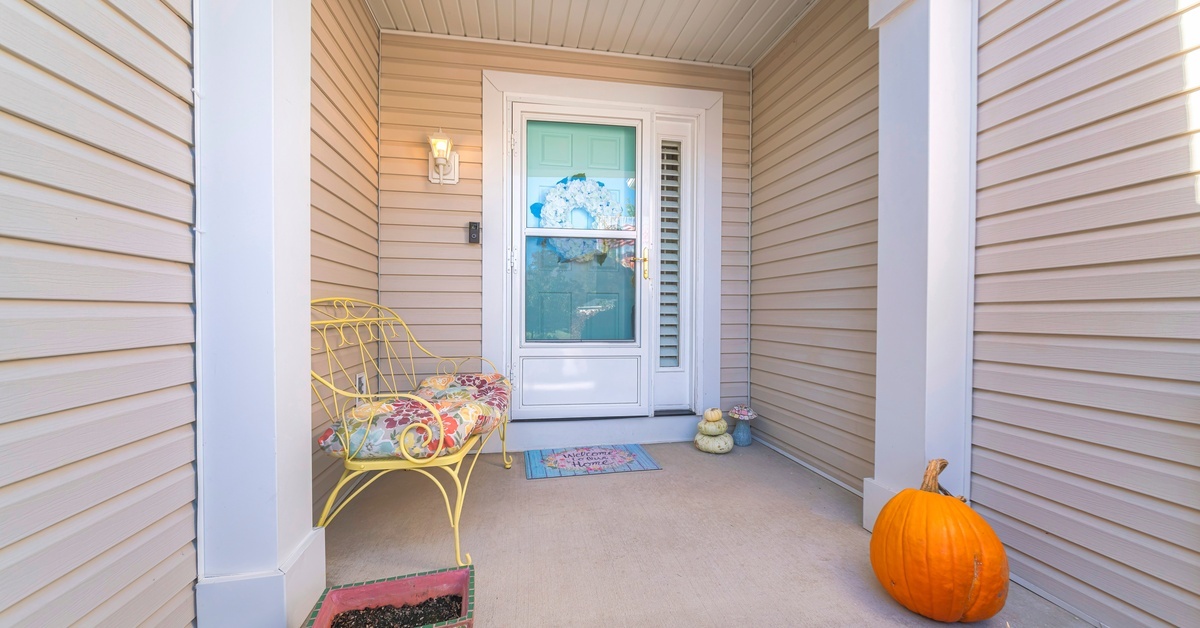 A storm door with glass panels that is closed with a blue-green front door behind it. There are pumpkins and a yellow bench outside of the door.