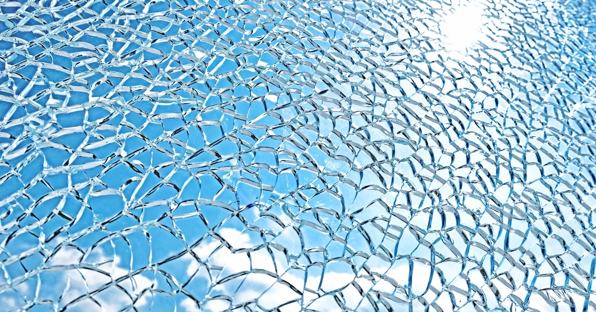 A pane of shattered glass. The blue sky and white clouds are clearly visible through the cracks.