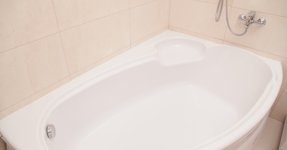 A wide, white bathtub with chrome fixtures is in a bathroom with large, tan tiles on the floor and wall.