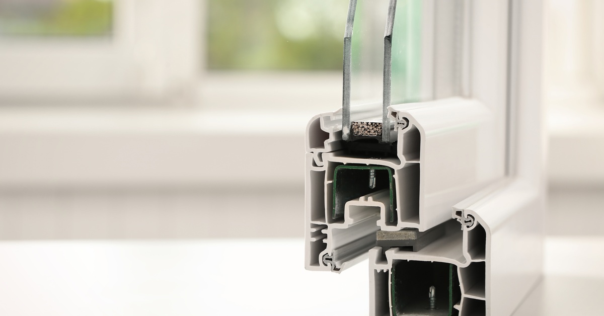 A double-pane window sample sits on a white sill, revealing its internal structure, with a window in the background.