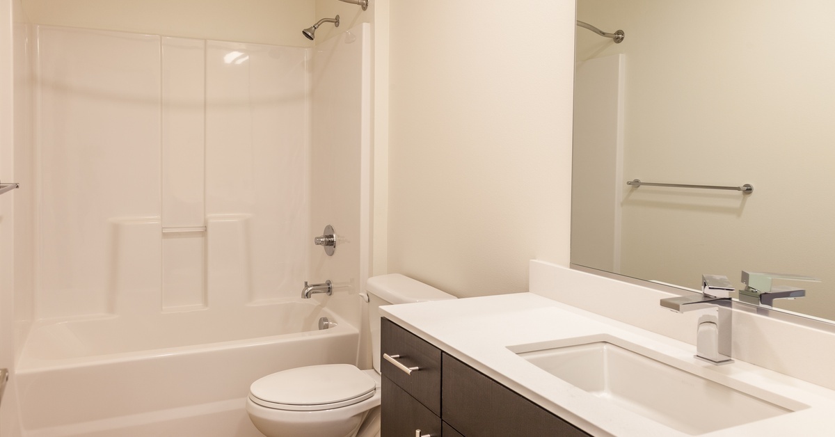 A plain, modern bathroom with a white, acrylic shower and tub surround. There's a stainless steel shower curtain rod.