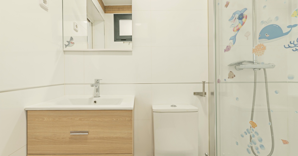Transform Your Small Mobile Home Bathroom With These Tips A close-up of a bathroom with a white toiler, a glass shower with stickers on it, and a floating wood vanity at the sink.
