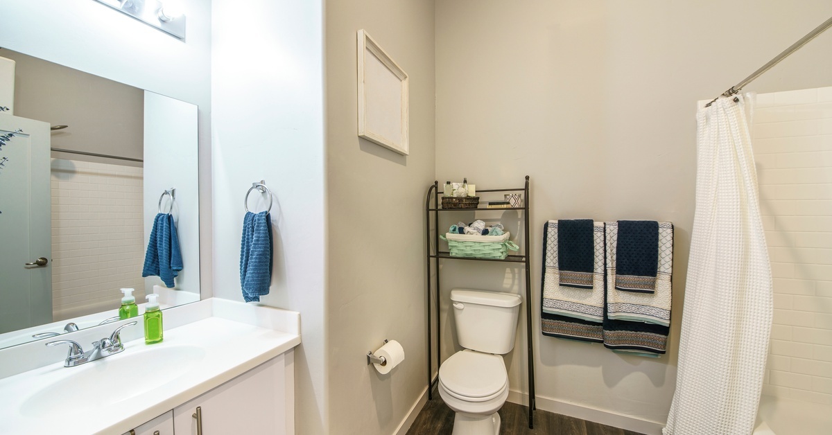 Transform Your Small Mobile Home Bathroom With These Tips A mobile home bathroom with a vertical shelf over the toilet for storage and a white shower curtain open to the tub.