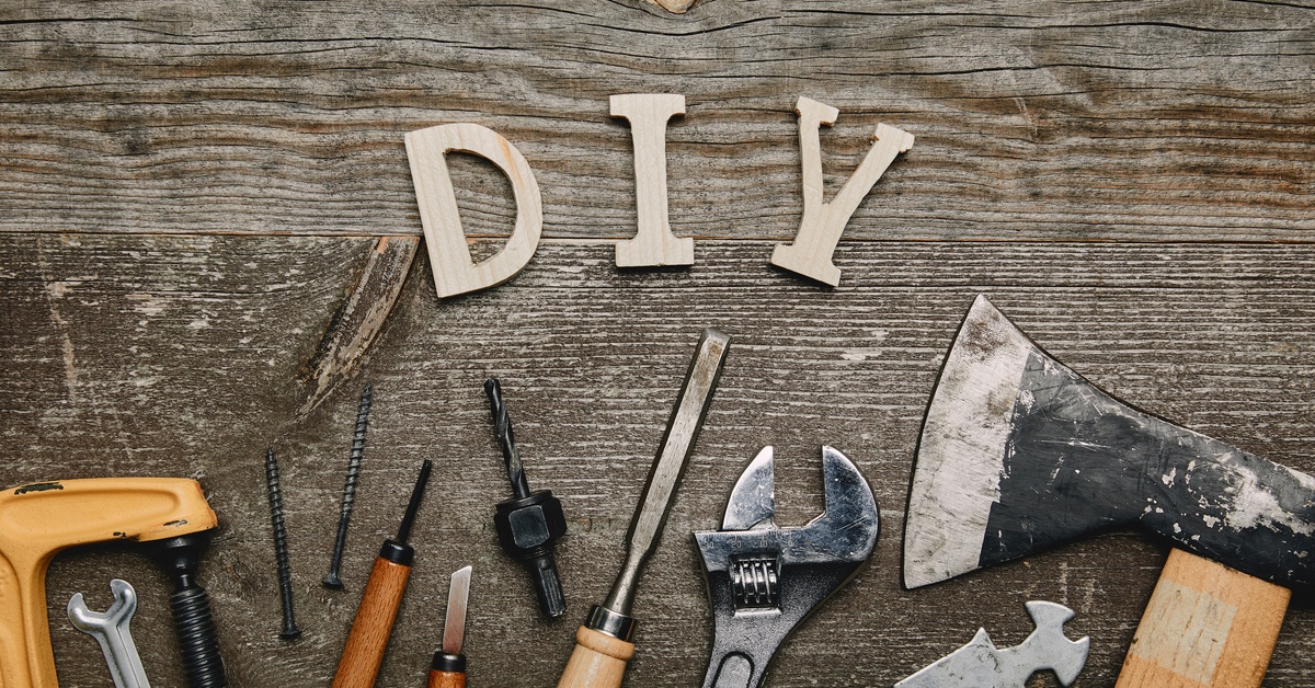 DIY letters on a weathered wood surface with assorted hand tools including a hammer, wrench, screwdrivers, and saw.