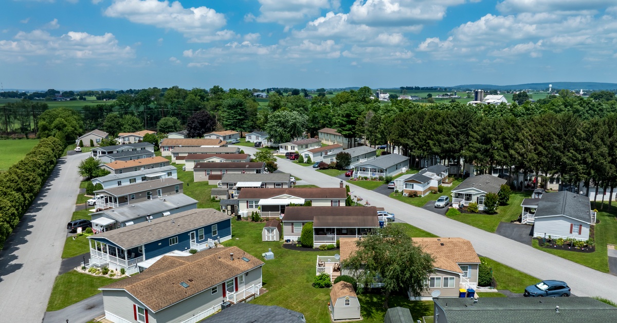 An aerial view of a mobile home community with neatly arranged manufactured homes, green lawns, and tree-lined streets.