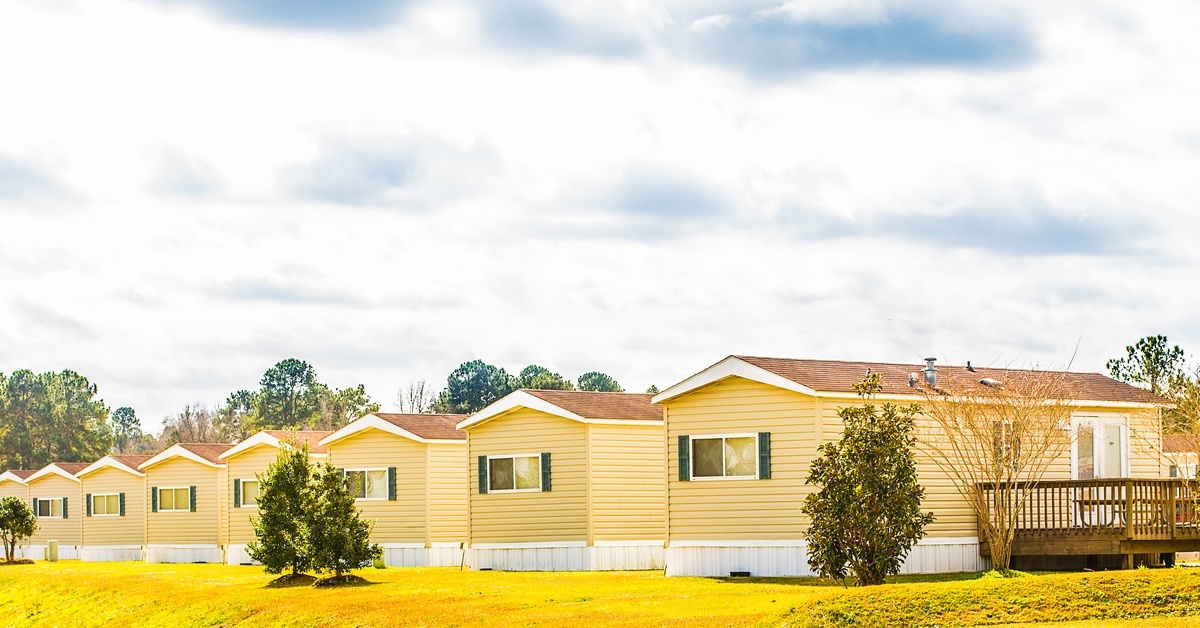A row of yellow manufactured homes set on grassy lots under a cloudy sky in a residential community.