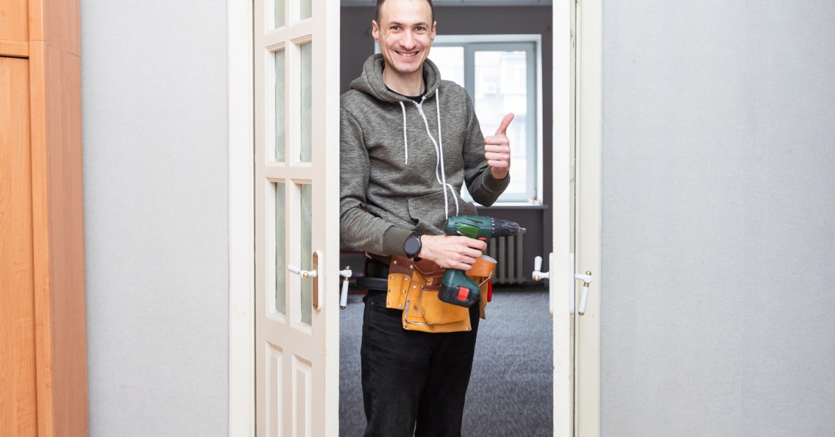 Simple Repairs for Common Mobile Home Door Problems A homeowner stands in an open doorway holding a power drill and giving a thumbs-up after completing door repair maintenance.