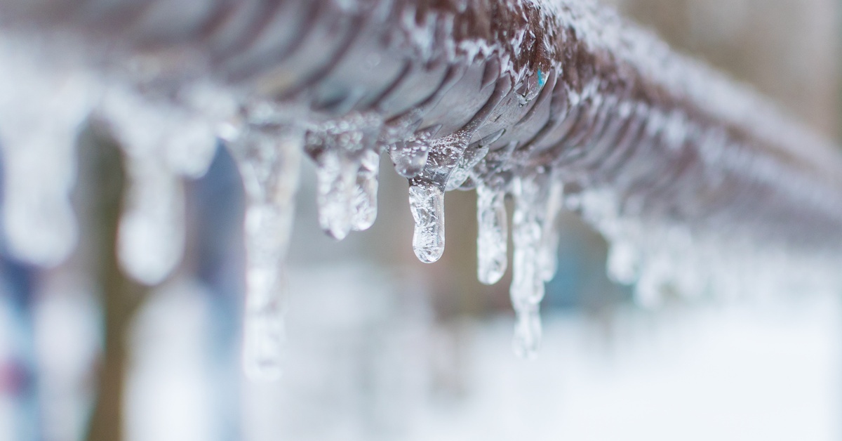 Icicles hang in varying lengths from a frozen pipe during winter, with a blurry, snow-covered background. Icicles hang in varying lengths from a frozen pipe during winter, with a blurry, snow-covered background.